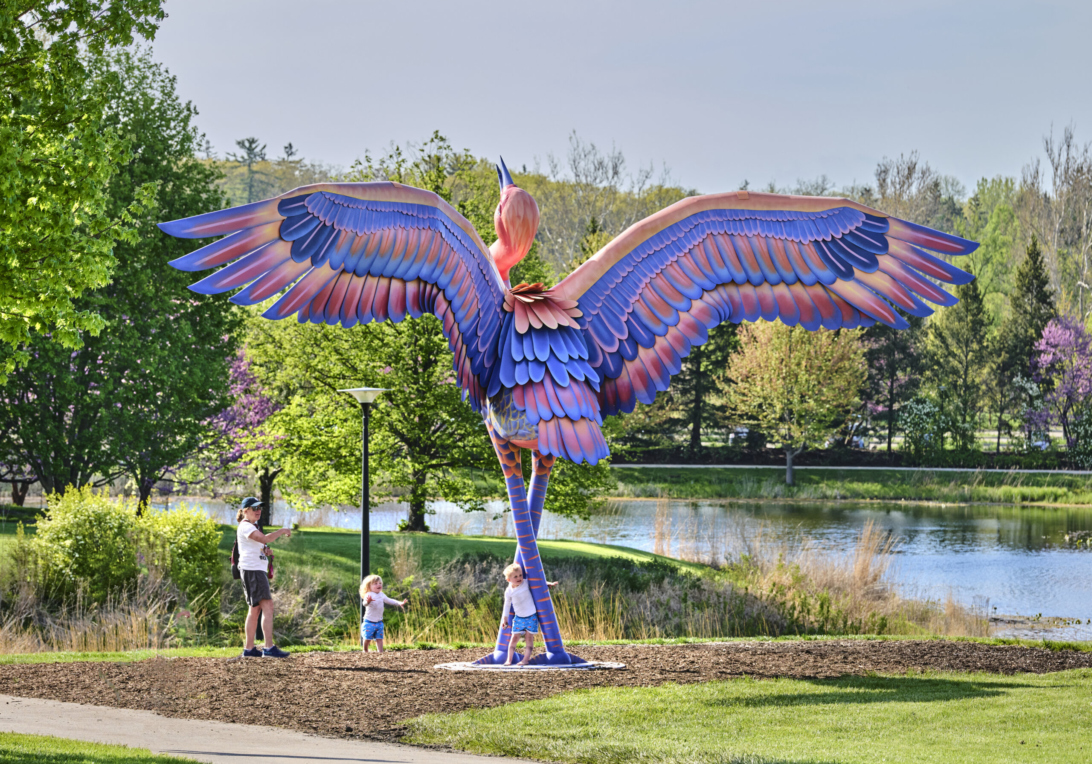 Photograph of a mother and two young children playing around Cadence a sculpture of a sandhill crane at The Morton Arboretum