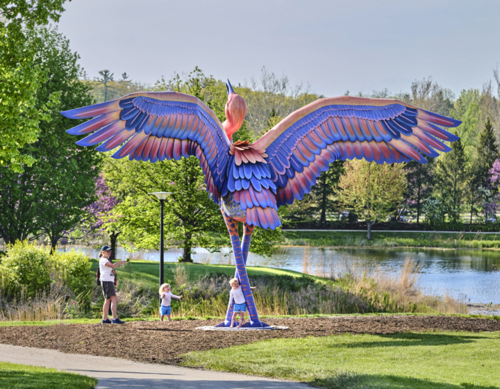 Photograph of a mother and two young children playing around Cadence a sculpture of a sandhill crane at The Morton Arboretum
