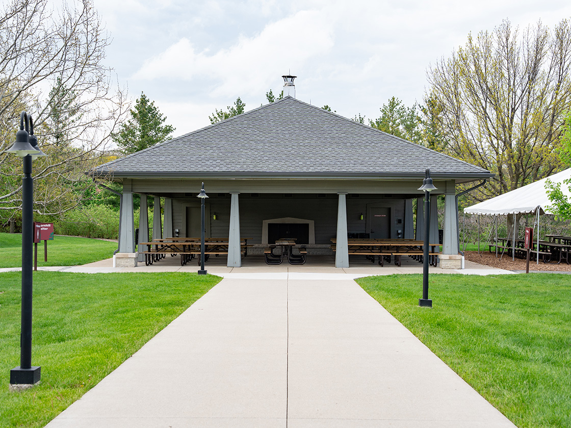 Photograph of the Thornhill Shelter structure with picnic tables and a nearby covered tent at The Morton Arboretum