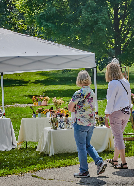 Photograph of visitors exploring a local artist tent at the Wine and Art Walk at The Morton Arboretum