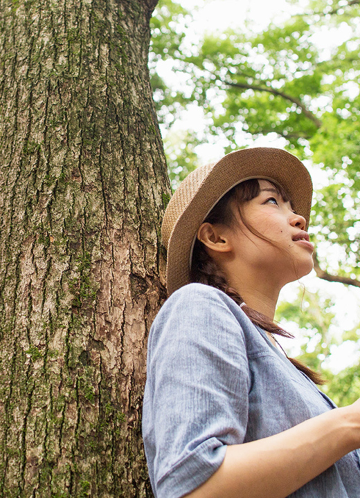 Photograph of a young woman holding a tablet standing below a forest canopy