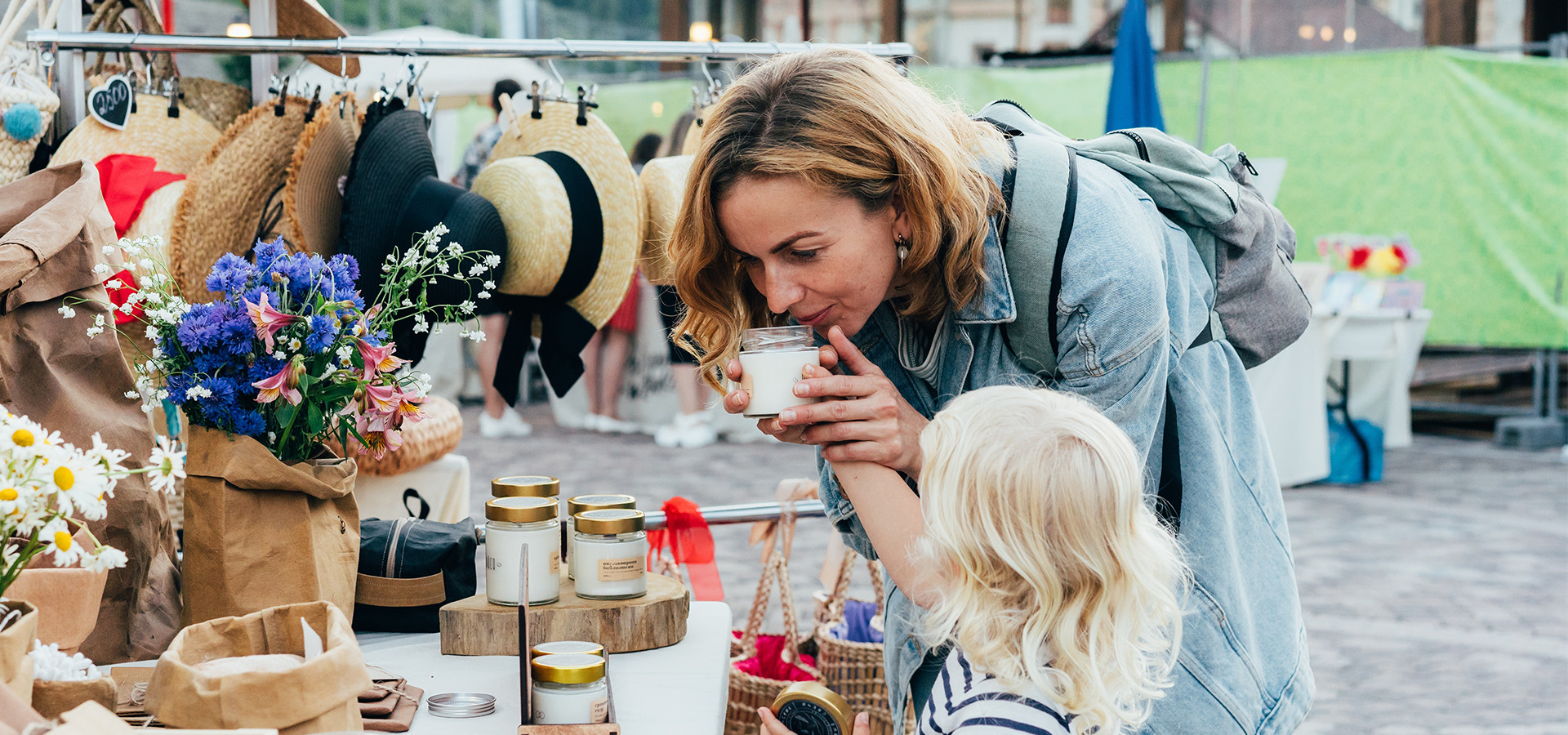 Photograph of a mother and a daughter smelling a scented candle at an open-air market