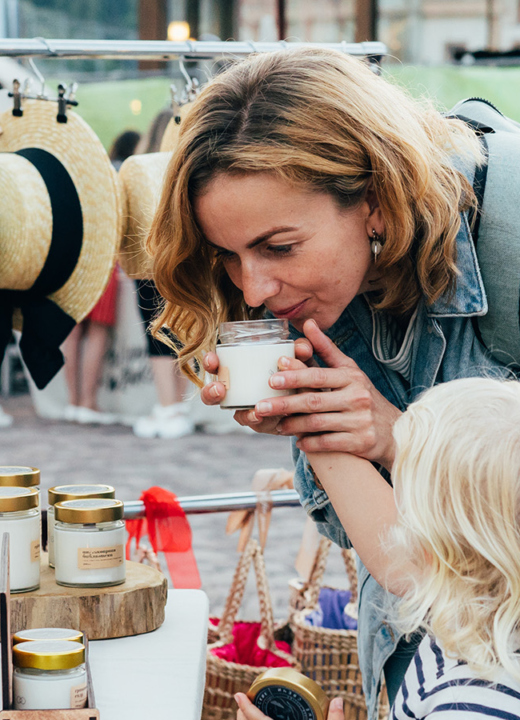 Photograph of a mother and a daughter smelling a scented candle at an open-air market