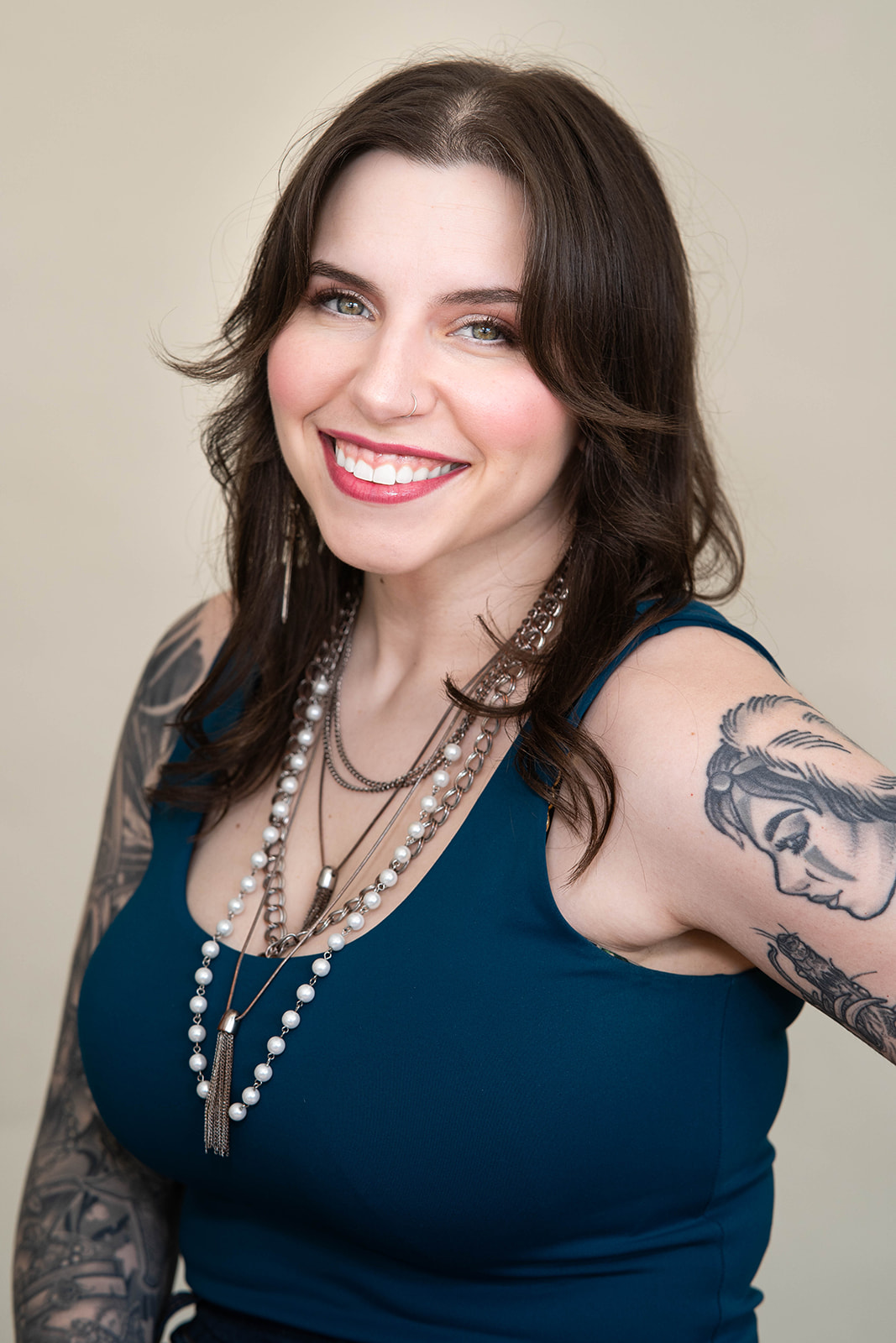 Headshot of woman wearing dark blue tank top and beaded jewelry, with a full sleeve of tattoos on her right arm