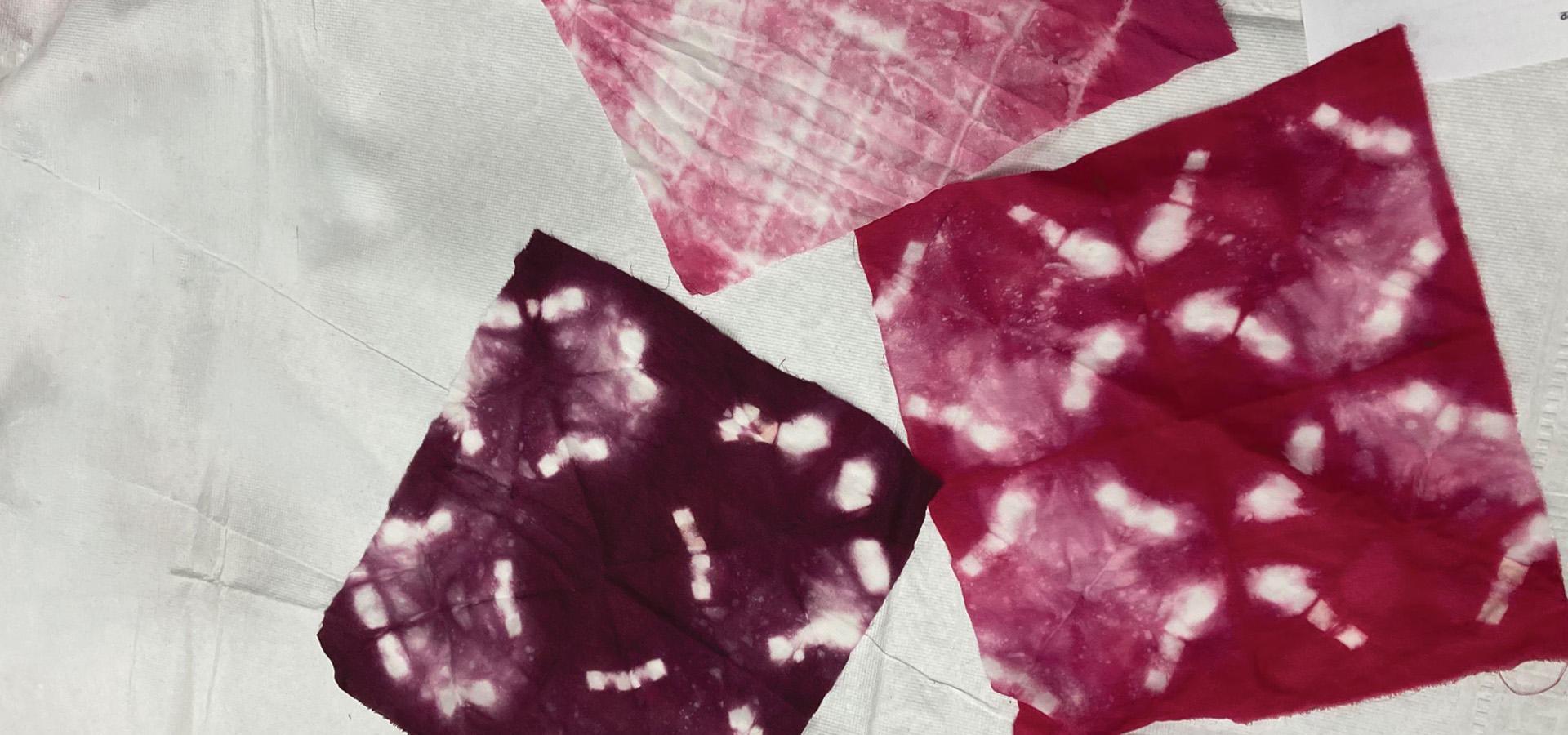 Squares of fabric dyed using Japanese tie-dye techniques with reddish-purple dye