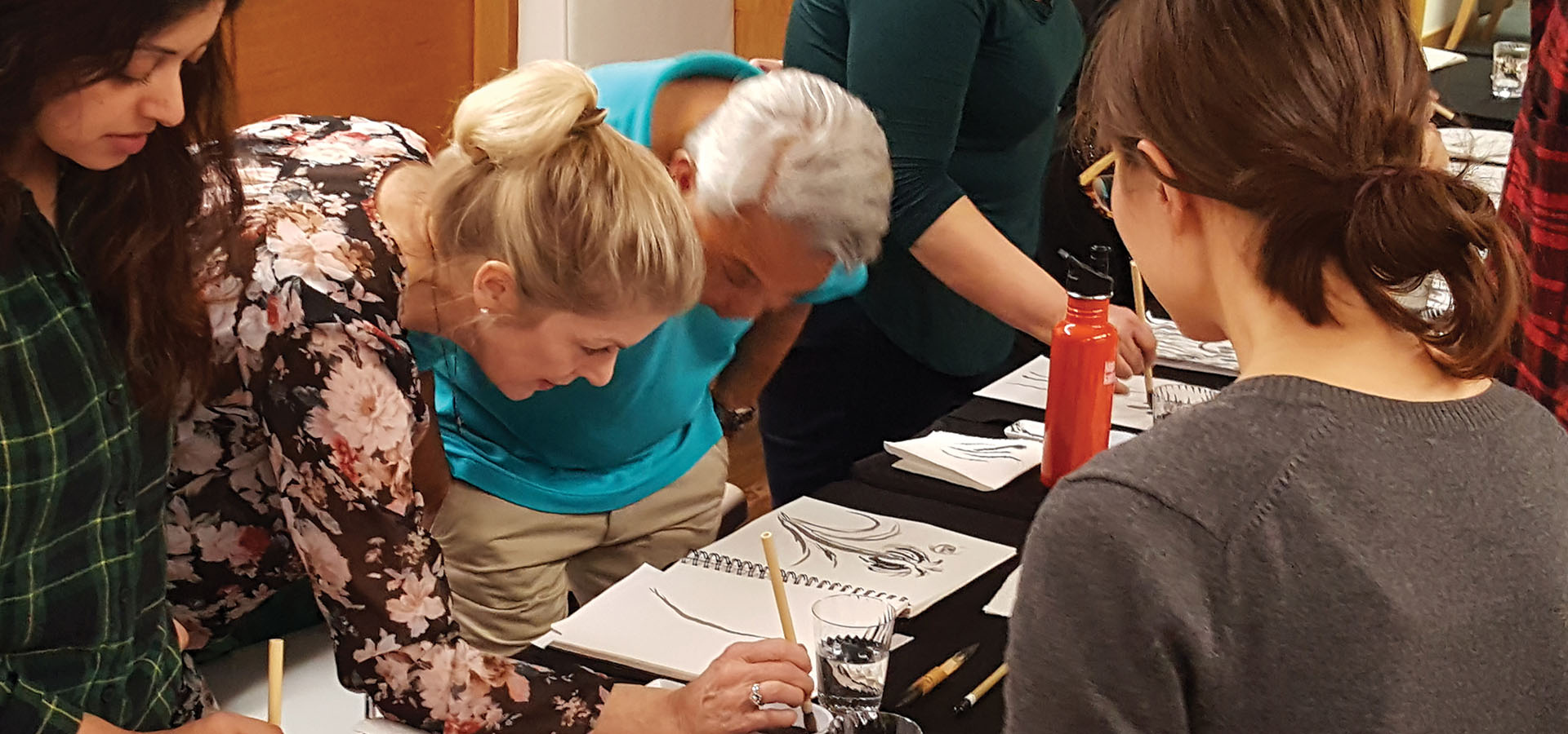 Artists stand at a table and use brushes to paint flowers in Sumi-e ink style