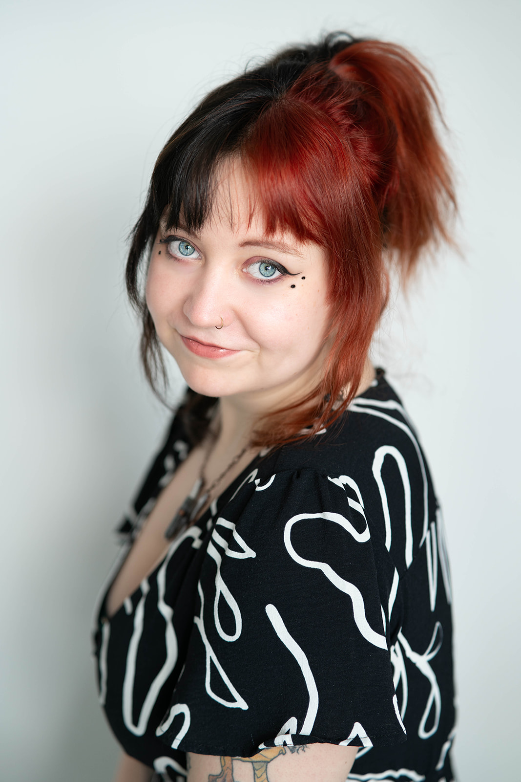 Headshot of woman with hair dyed half red, half black, wearing black dress with white line art design