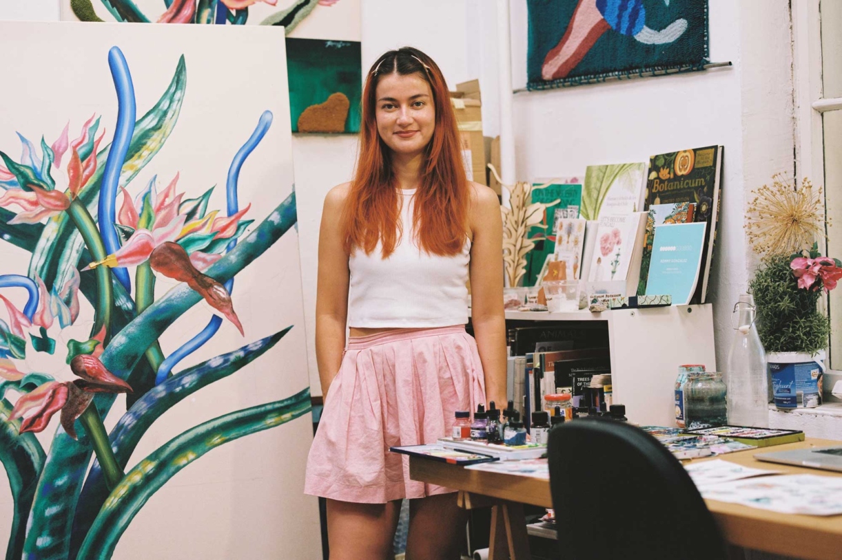 A portrait of artist Rommy Gonzalez in front of all her botanical artwork