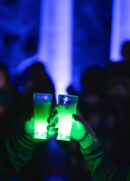 Two people make a toast with green light-up glasses