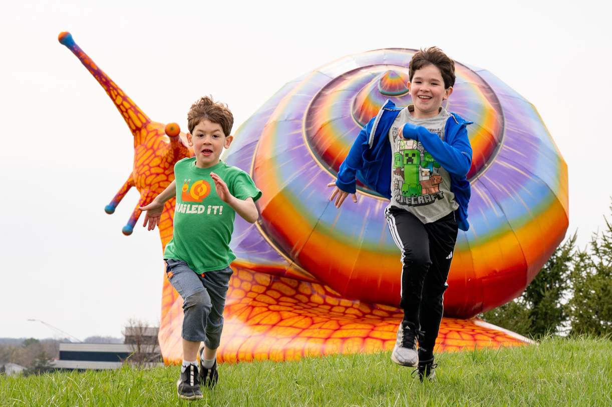 Two boys smiling as they run from a large snail sculpture