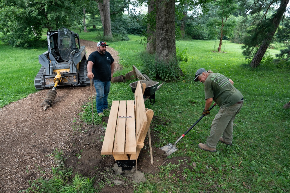 Two people dig holes to install a tribute bench.