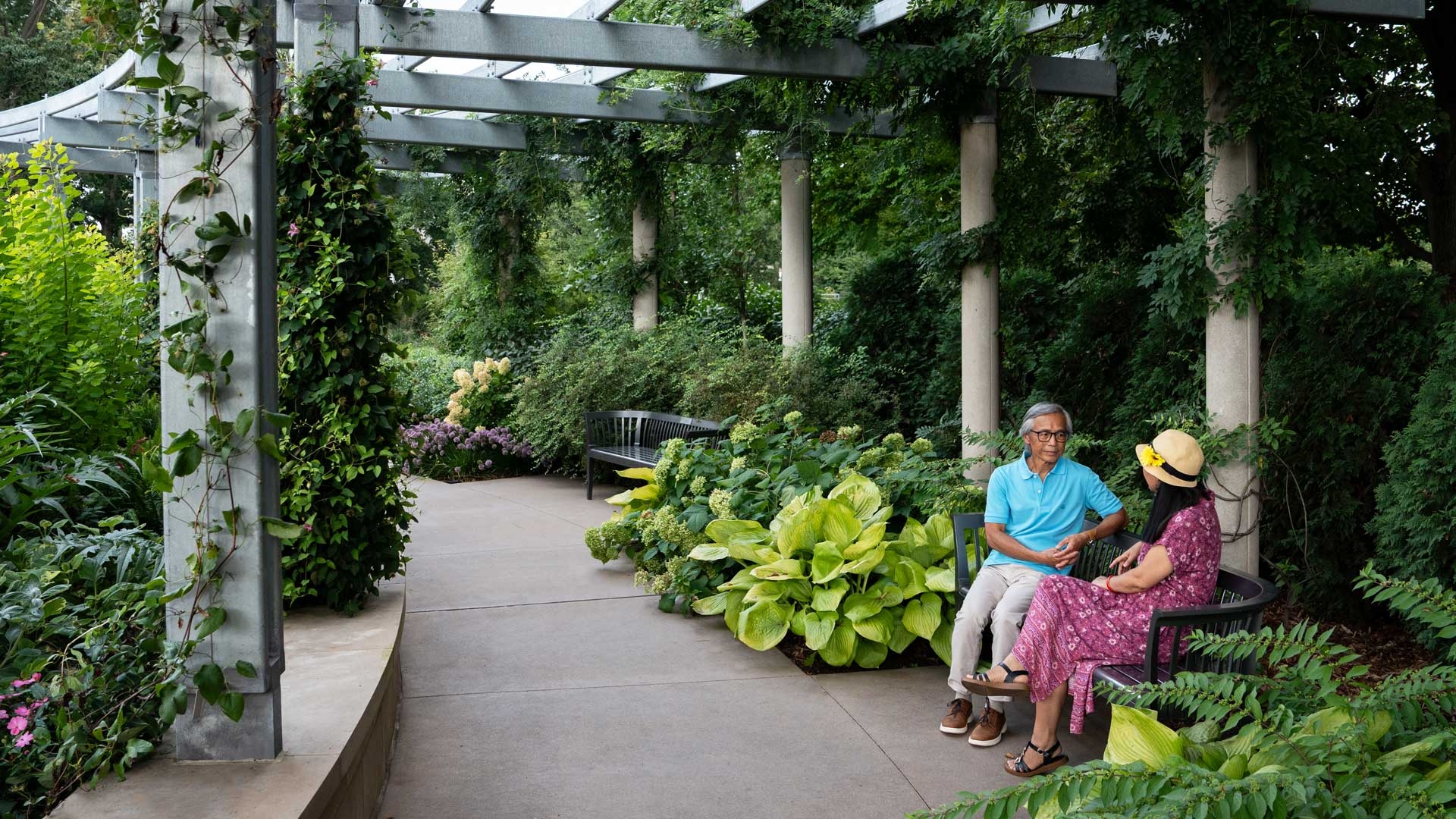 A couple sits on a bench in the Grand Garden surrounded by lively plants and blooms