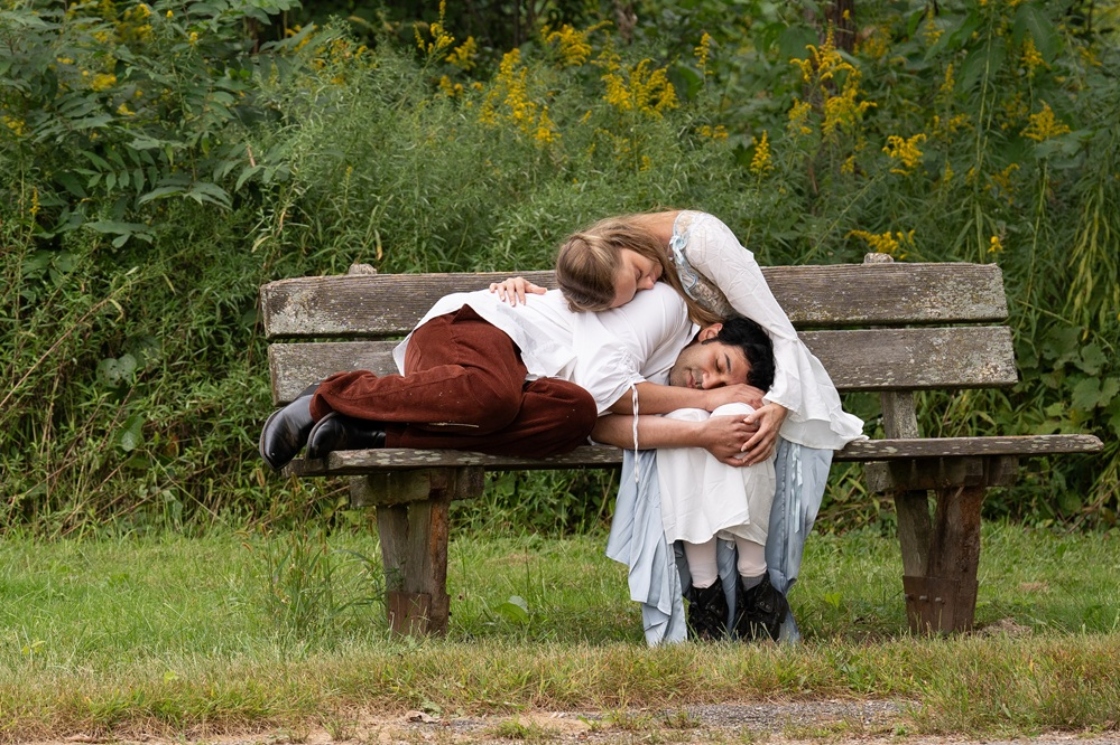 Heathcliff reads his head in Katherine's lap on a weathered bench in front of wildflowers